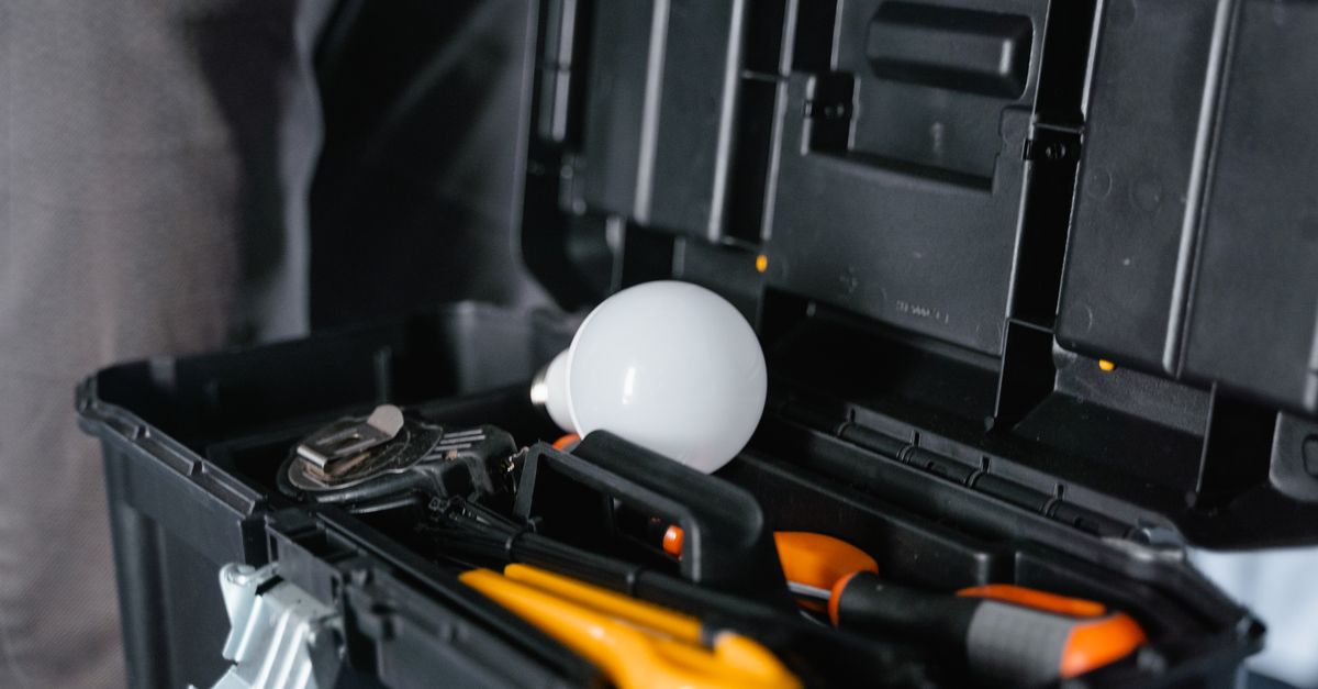 Caisse à outils ouverte avec marteau, tournevis, mètre ruban et perceuse-visseuse posés sur un établi en bois