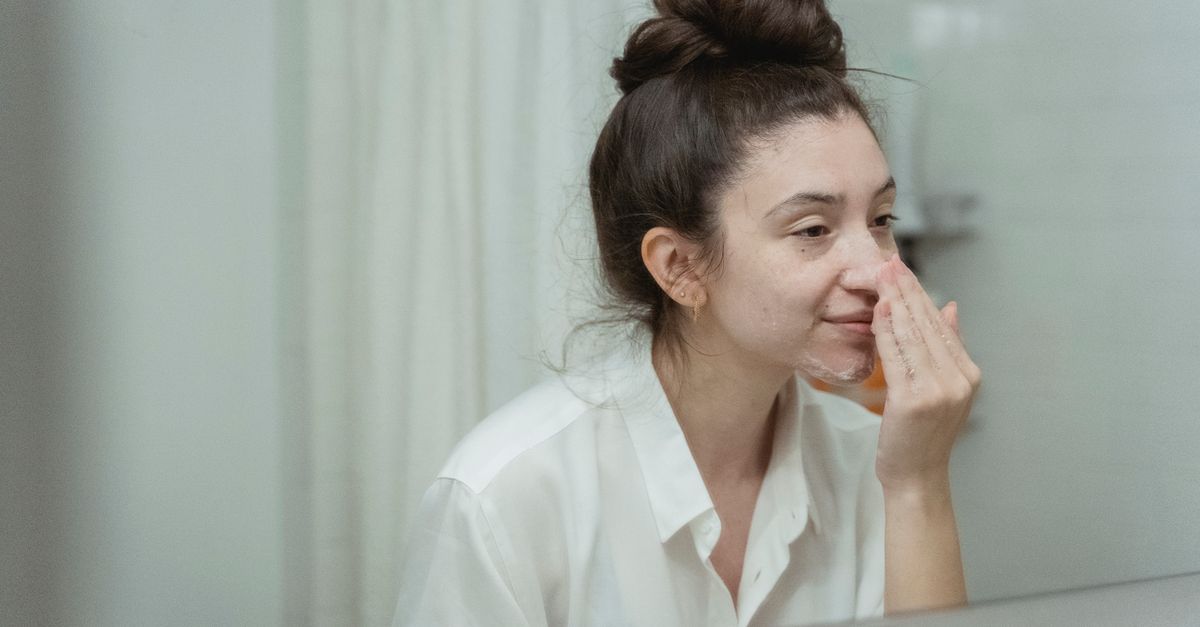 Femme appliquant un soin pour peau grasse devant un miroir
